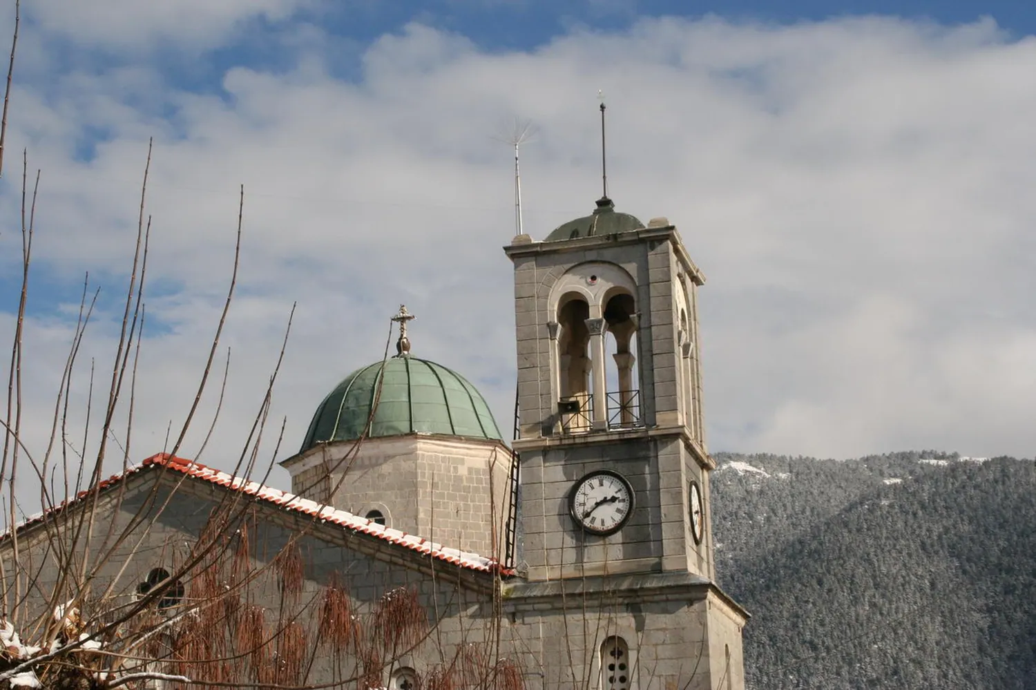 Εκκλησία με πέτρινο καμπαναριό και ρολόι, με βουνό πίσω