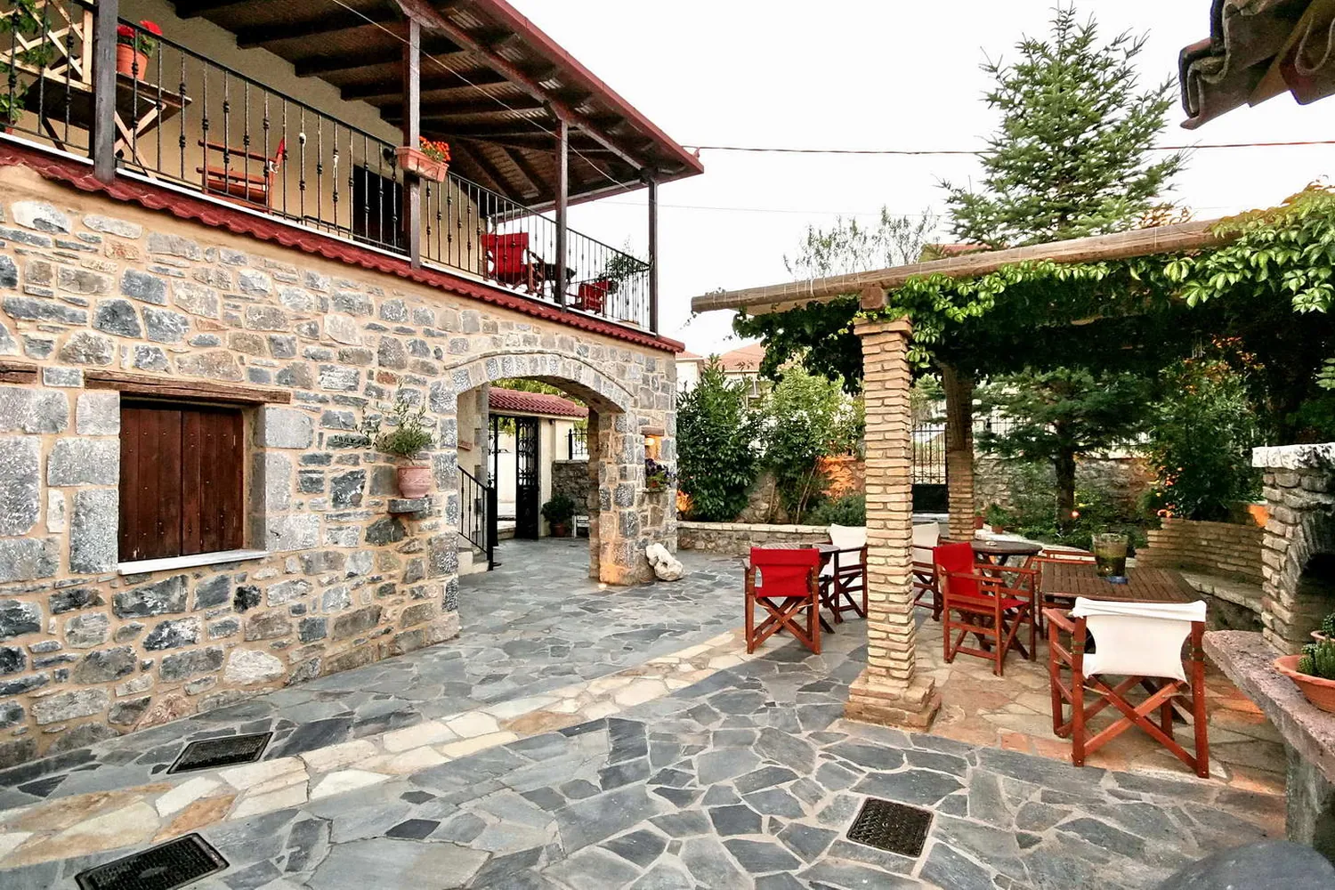 Η πλακόστρωτη αυλή με την κληματαριά και τις κόκκινες καρέκλες